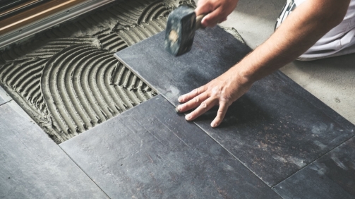 Worker carefully placing ceramic floor tiles on adhesive surface