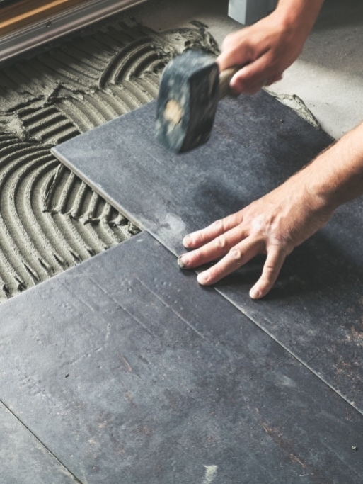 Worker carefully placing ceramic floor tiles on adhesive surface
